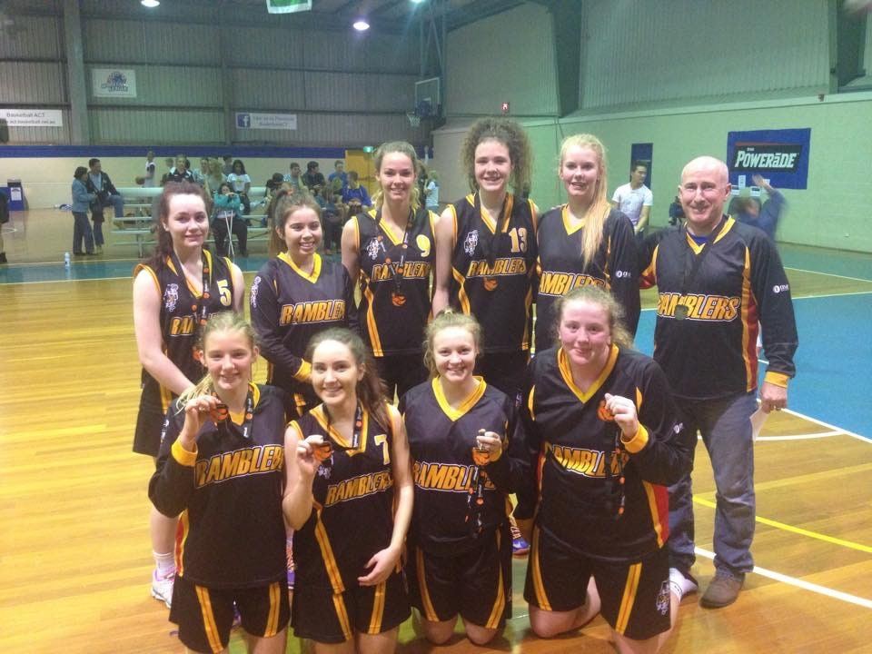 A Ramblers junior girls' team pose together in black and gold with their medals and coach after a grand final.