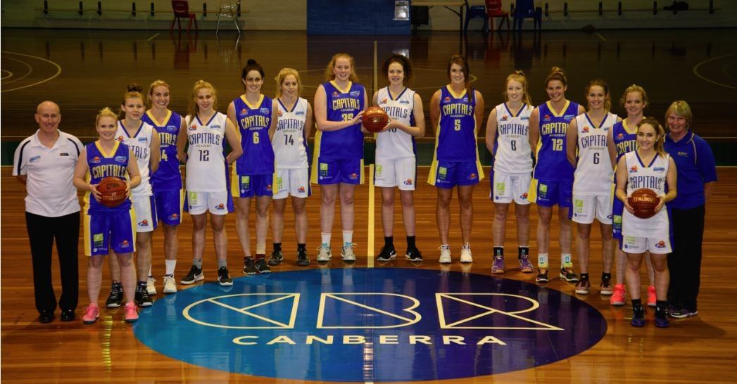The Canberra Capitals Academy team pose together at centre court, some players holding basketballs.