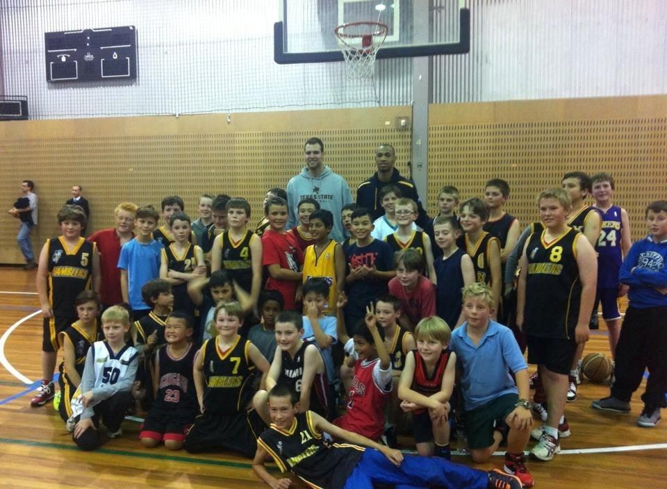 A large group of Ramblers junior boys crowd around two Canberra Gunners import players on the court after a shooting clinic.