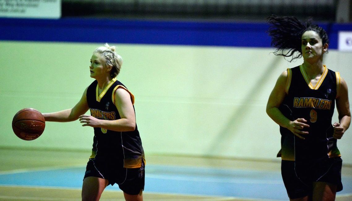 Two Ramblers Premier Women players in black and gold, one dribbling the ball, running down the court.