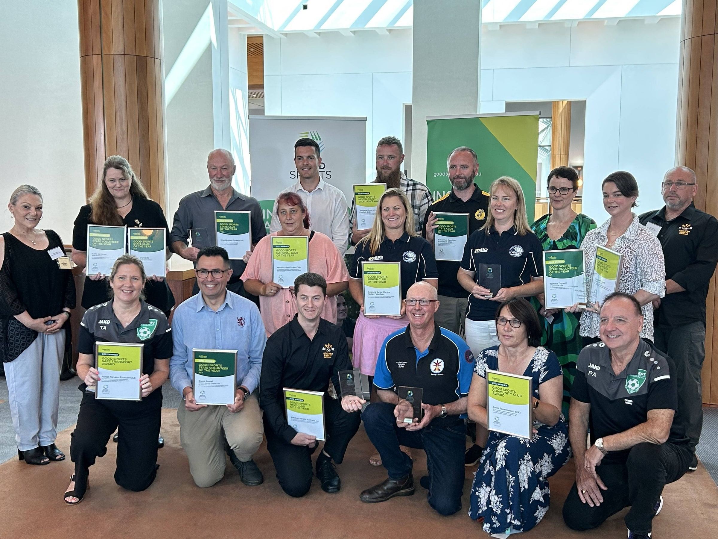 A large group of award winners and volunteers from multiple ACT sporting clubs pose together holding their certificates and trophies.