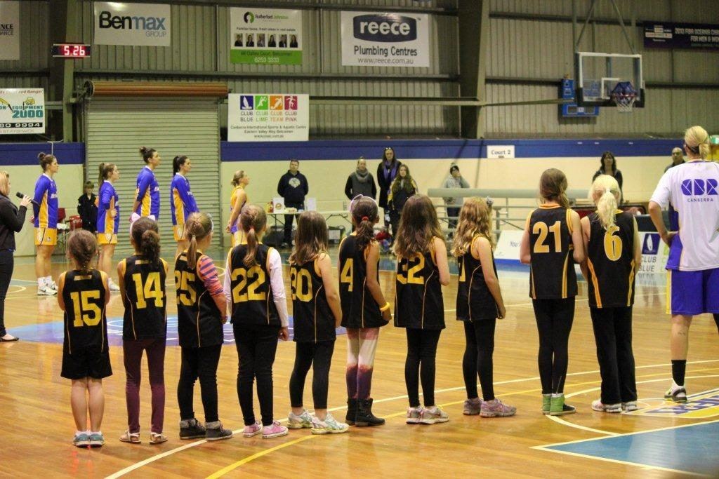 Ramblers junior girls in black and gold line up on court forming a guard of honour for the Canberra Capitals Academy players.