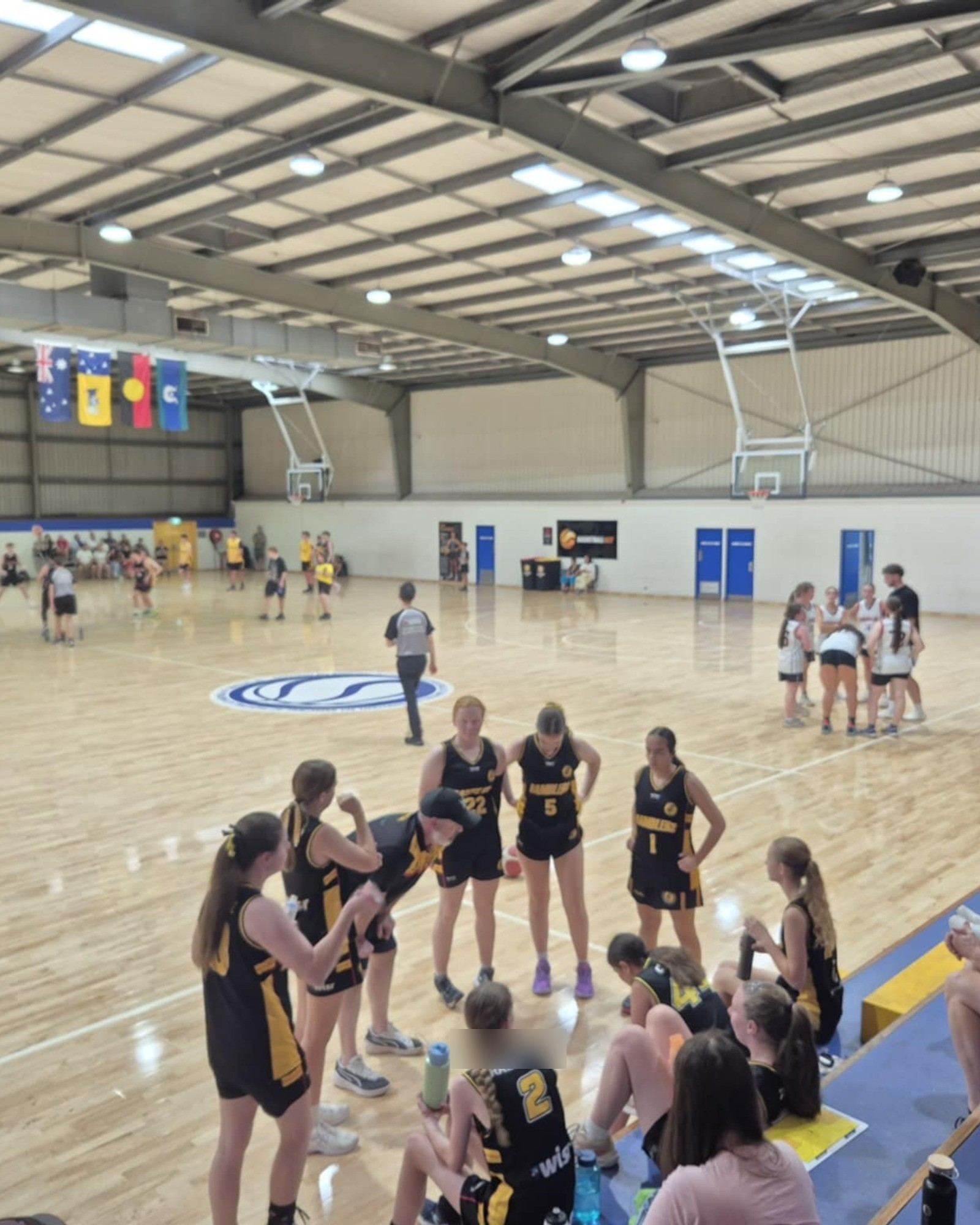 Ramblers players huddle together on court before a game, teammates and family watching on
